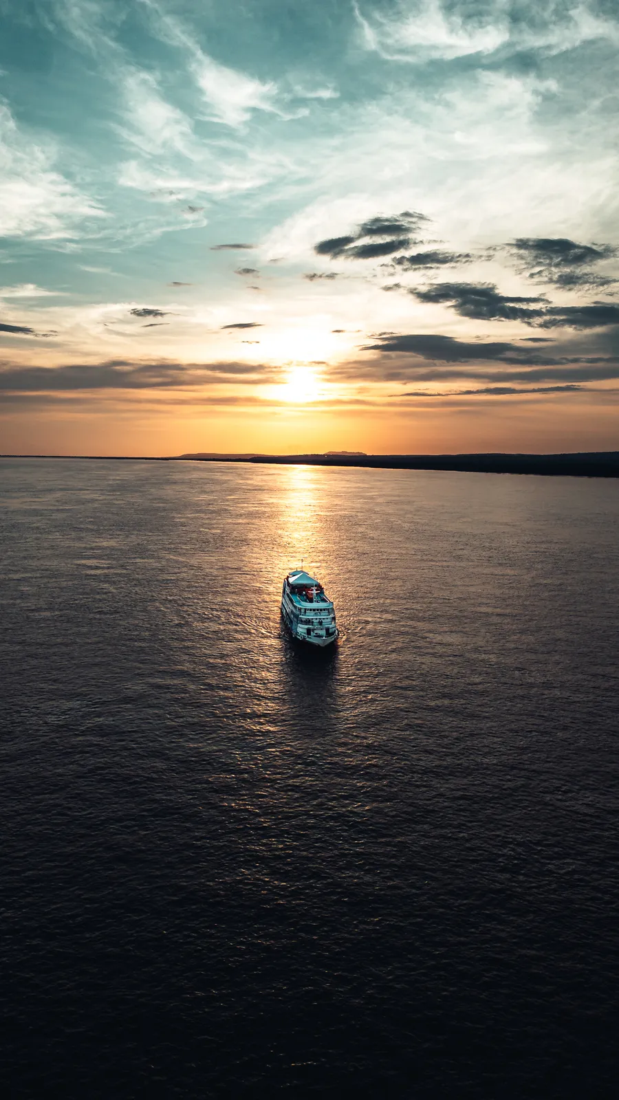 Barco navega rumo ao pôr do sol em um grande rio, visto de cima