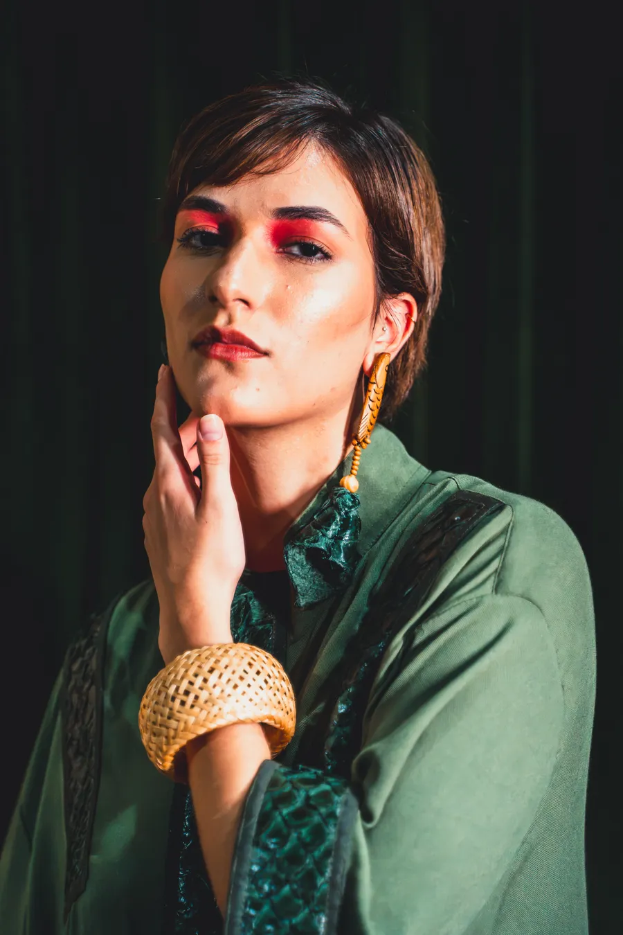 Retrato de modelo com maquiagem vermelha, brinco de peixe e bracelete de palha trançada